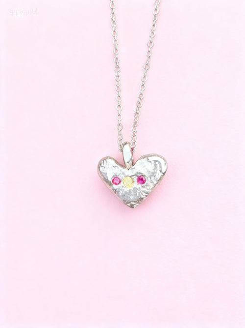 Silver-toned heart pendant necklace with floral details and pink and pale-yellow accents on a pink background